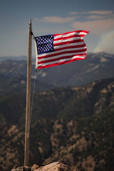 The flag ripping in a 35 mph plus west wind moments before Clayton lowered it.  On the horizon, the Cascade Complex fire burns 18 miles northwest of Challis.
