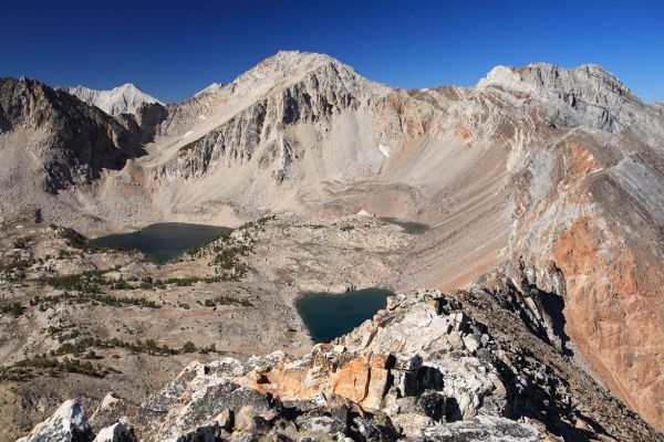 The foreground ridge descends to the Gunsight, and then ascends to Peak 11238, forming the east flank of the Chinese Wall.  Peak 11238 anchors the 90 degree corner of the Chinese Wall.  In the center, rising above between Tin Cup and Gunsight Lakes is Calkens Peak.
