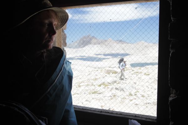 Hiker, as viewed through reinforced window, approaches Muir Hut.
