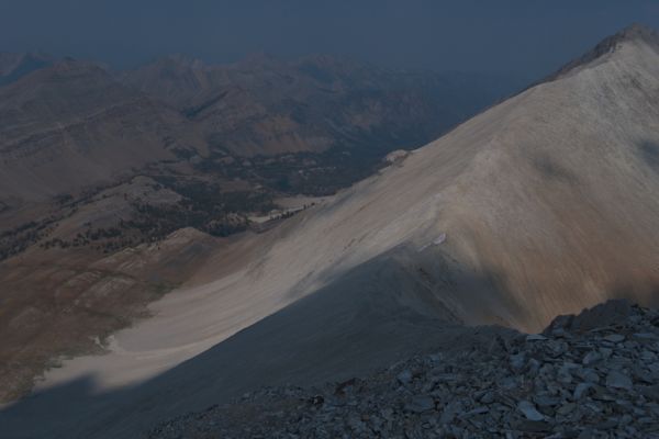 The view north to the saddle, bisected by the shadow of a passing cloud, half the brilliant white sedimentary limestone still in sunlight.
