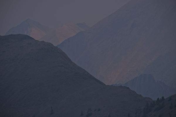 As seen from the saddle south of Strawberry Basin, the Warm Springs Creek drainage plunges deeply behind the east wall of Strawberry Basin.  Beyond, to the northeast, the White Cloud Peaks rise in the haze.
