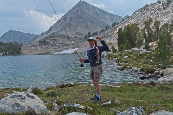 A rare shot of the author holding the one that didn’t get away.  A rainbow about the same size broke the line where the tippet met the leader in a few inches of water, and headed for deep water, taking my grasshopper dry fly with him!  After tying on a new leader, adding tippet, and tying another grasshopper to the end of the tippet—a project which takes me much longer than it should—I hooked into this rainbow on the first or second cast.  Needless to say, I was extremely careful about landing the fish.
