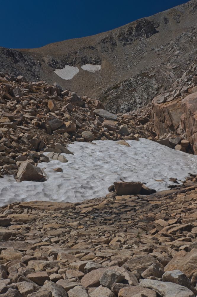 The objective is the saddle below the skyline, above those two patches of snow.  I find it easiest to climb on the more solid terrain, ascending as high as possible (right edge of frame), then contour over to the saddle.  Reaching the saddle is the crux, due to the loose scree.
